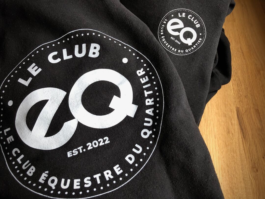 Detail of two Le Club EQ Hoodies in black with white logo laying on top of each other