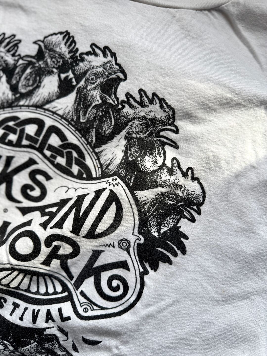 Detail of illustrated crowing roosters on a white t-shirt text reading "Cocks and Clogwork" Steampunk Festival.