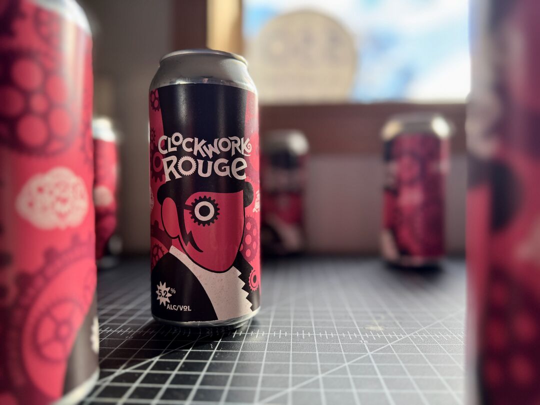 Clockwork Rouge beer cans arrayed on work table. Labels show a graphic styled ringmaster in front of exploded clock and cog mechanical parts on a salmon coloured field.