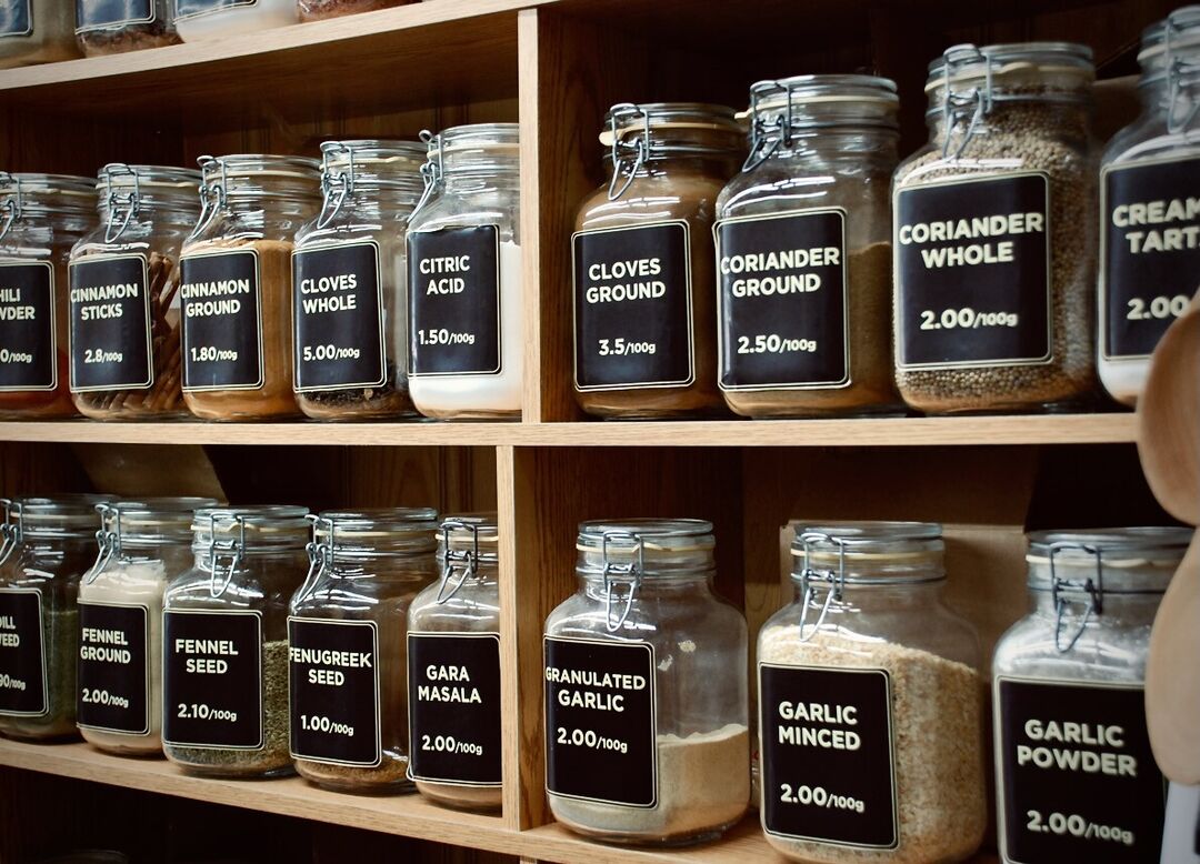 Two shelves of jars containing spices with signs like "GARAMSAH" and "CURRY POWDER".