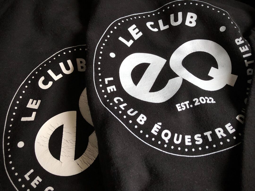 Detail of two Le Club EQ Hoodies in black with white logo laying on top of each other
